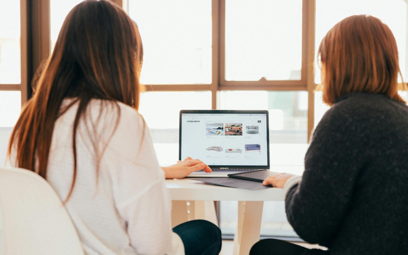 two women talking while looking at laptop computer by KOBU Agency courtesy of Unsplash.