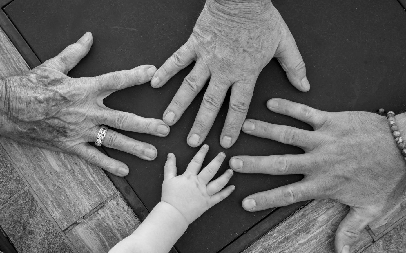 Four hands of different ages reaching towards center by Barnabas Piper courtesy of Unsplash.