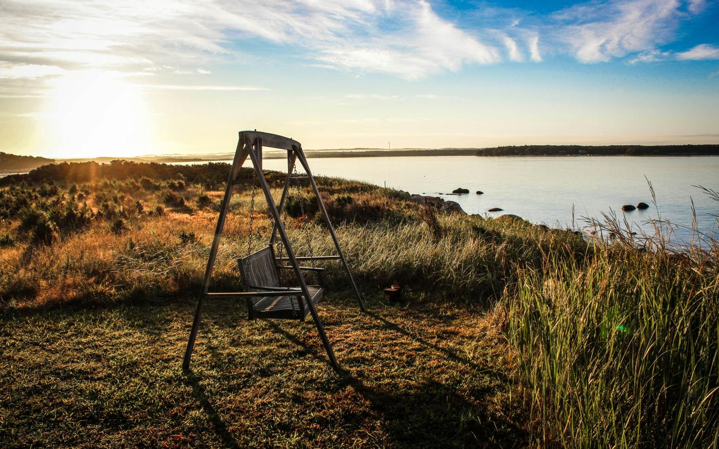 gray wooden bench swing facing body of water surrounded by grass by Jon Eckert courtesy of Unsplash.