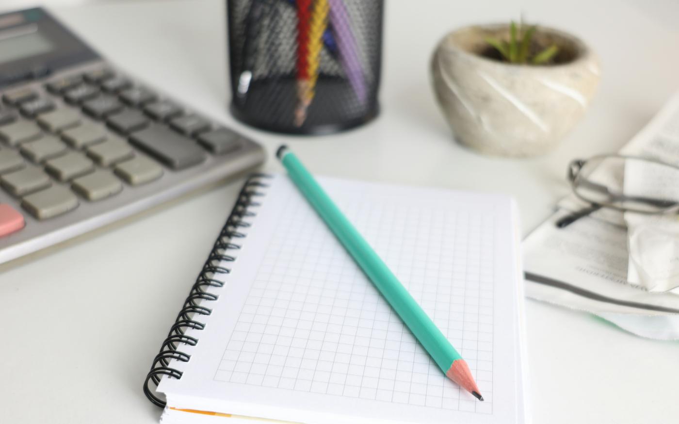 Desk with calculator, notebook, pencil, and plant. by Cht Gsml courtesy of Unsplash.