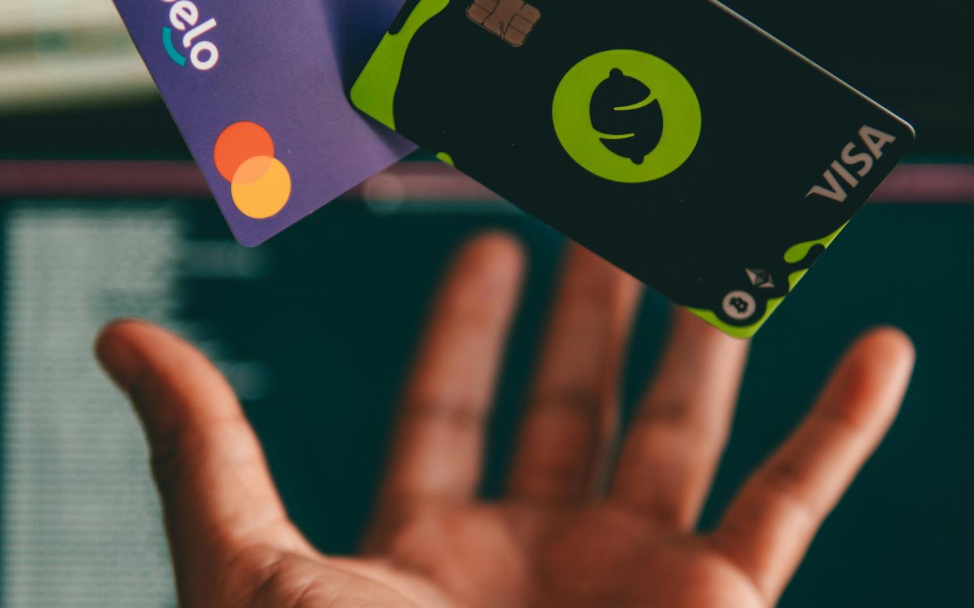 a hand holding a credit card in front of a computer by Diego Gennaro courtesy of Unsplash.