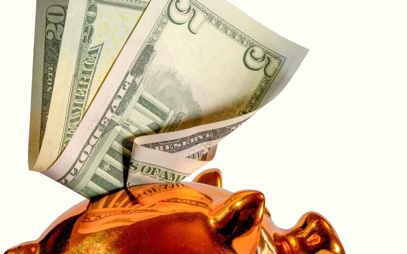 Us dollar bills being inserted into a piggy bank by Markus Kammermann courtesy of Unsplash.