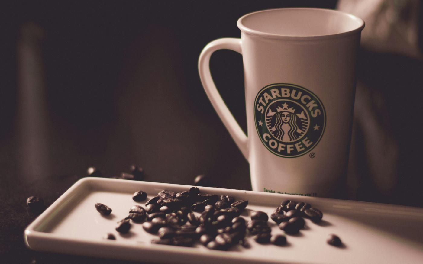 coffee beans beside Starbucks coffee mug by Hans Vivek courtesy of Unsplash.
