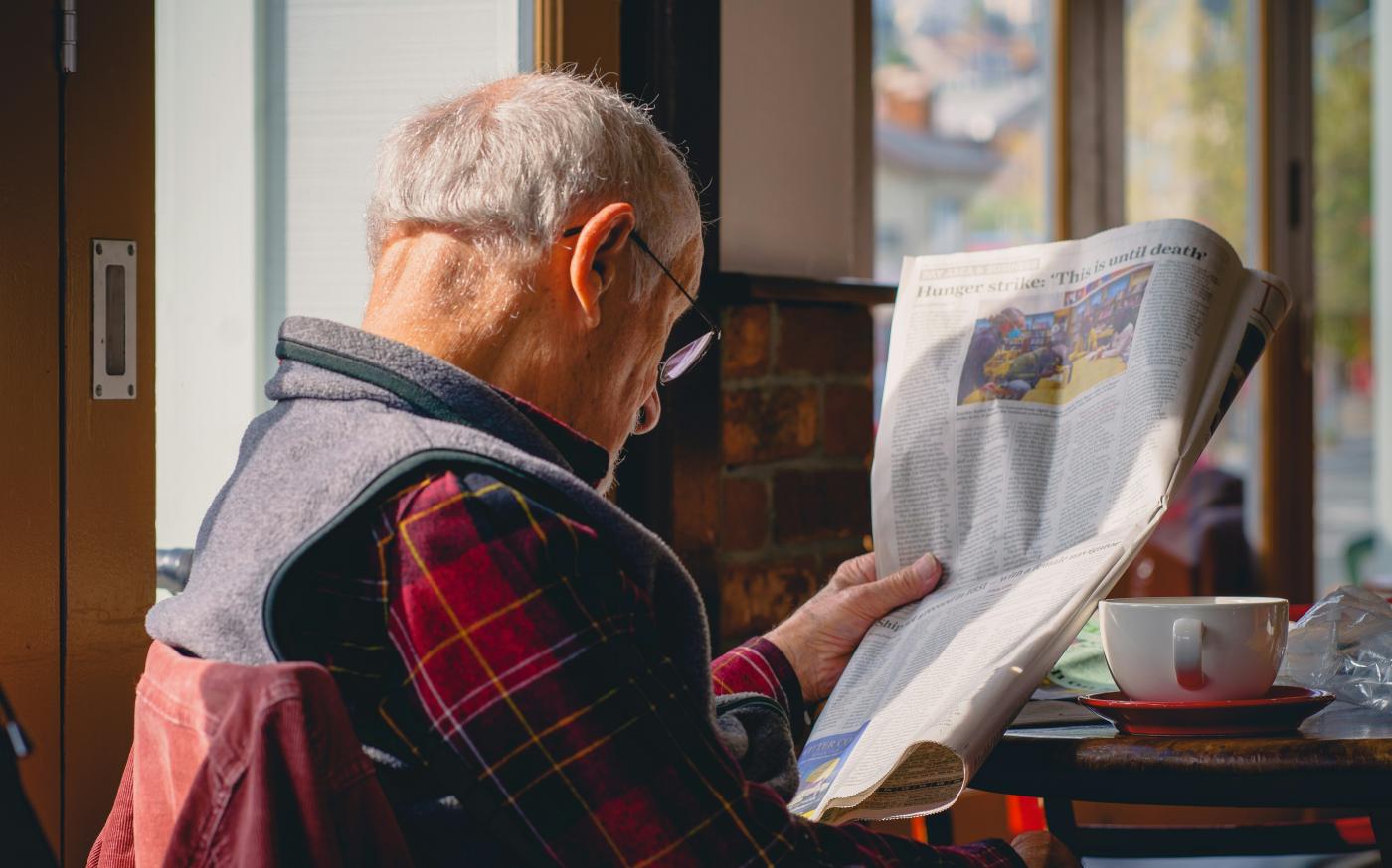 a man sitting at a table reading a newspaper by Joseph Sintum courtesy of Unsplash.