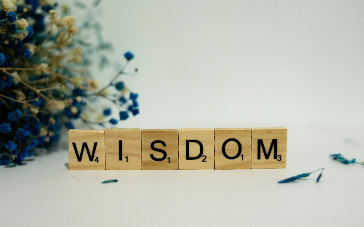 a wooden block spelling the word wisdom next to a bouquet of flowers by Alex Shute courtesy of Unsplash.