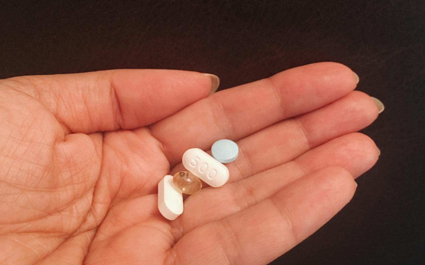 person holding four assorted medicine tablets by pina messina courtesy of Unsplash.