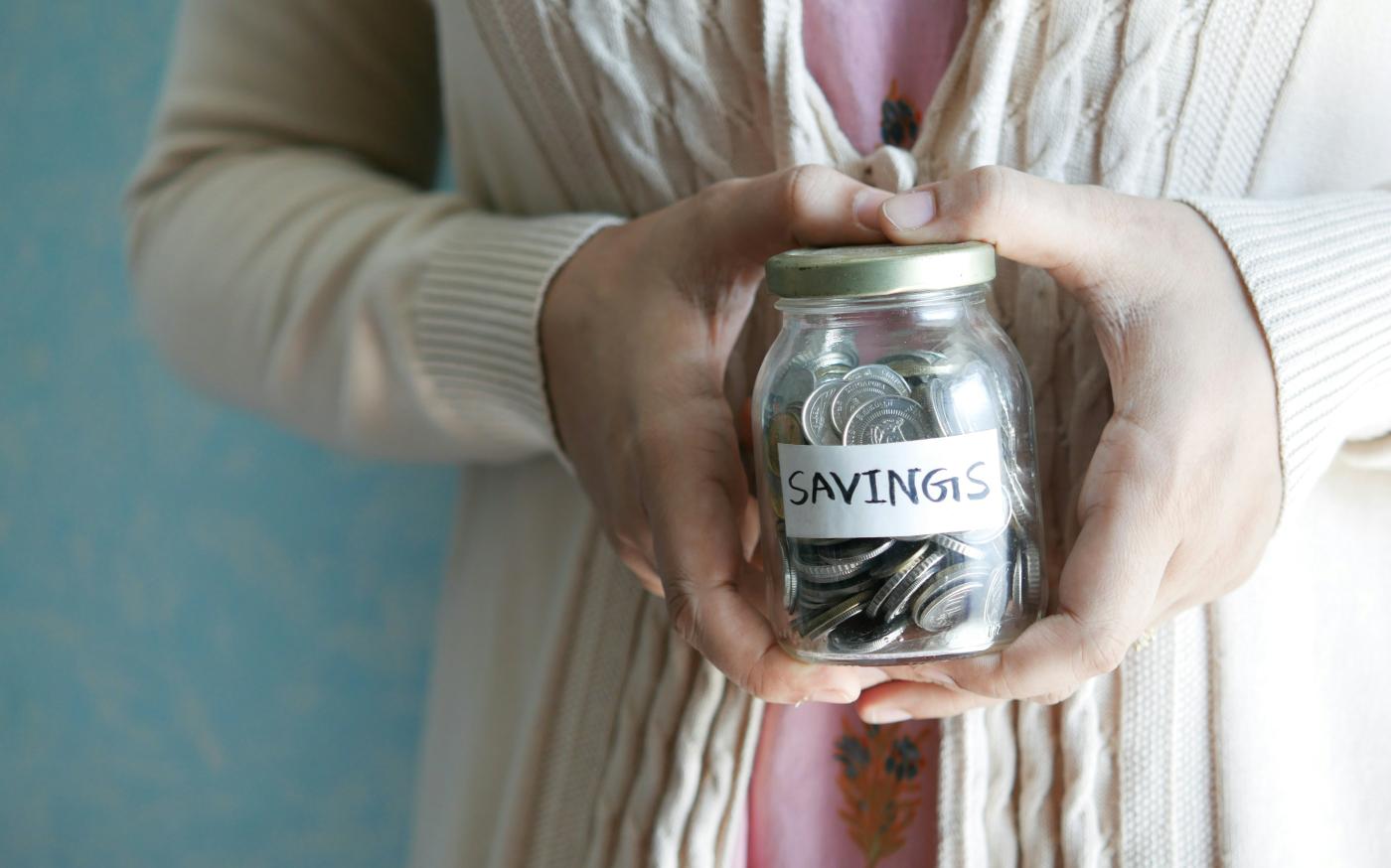 a woman holding a jar with savings written on it by Towfiqu barbhuiya courtesy of Unsplash.