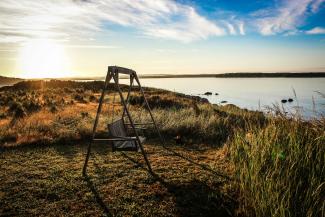 gray wooden bench swing facing body of water surrounded by grass by Jon Eckert courtesy of Unsplash.