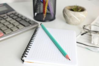 Desk with calculator, notebook, pencil, and plant. by Cht Gsml courtesy of Unsplash.
