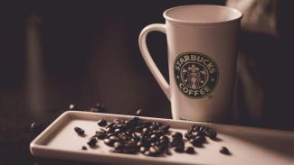 coffee beans beside Starbucks coffee mug by Hans Vivek courtesy of Unsplash.