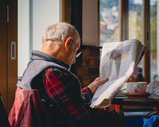 a man sitting at a table reading a newspaper by Joseph Sintum courtesy of Unsplash.